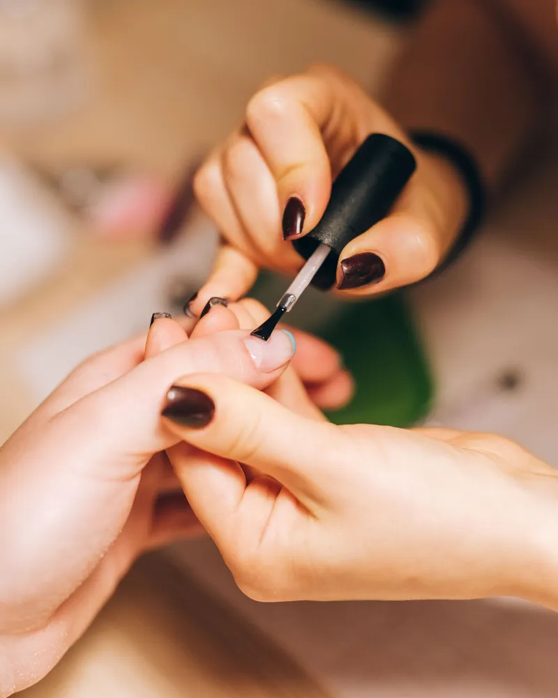 Application d'un vernis prune au pinceau sur les ongles d'une cliente